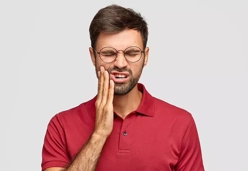 endodontie-berlin-kudamm Ein Mann hält schmerzversehrt seine Wange