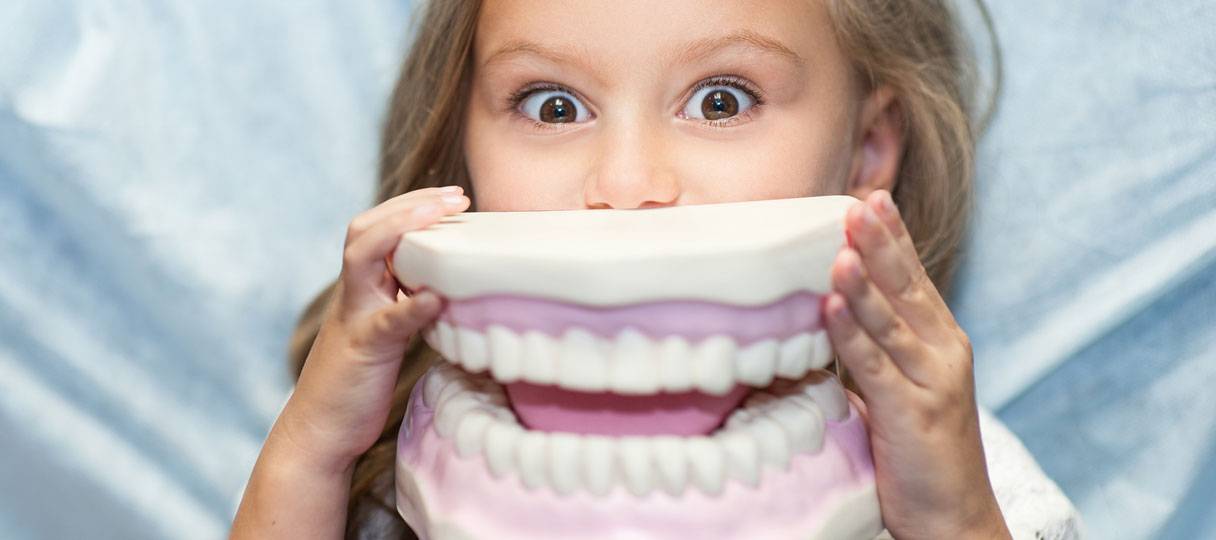 Ein Kind hält sich den Gipsabdruck eines Gebisses vor den Mund